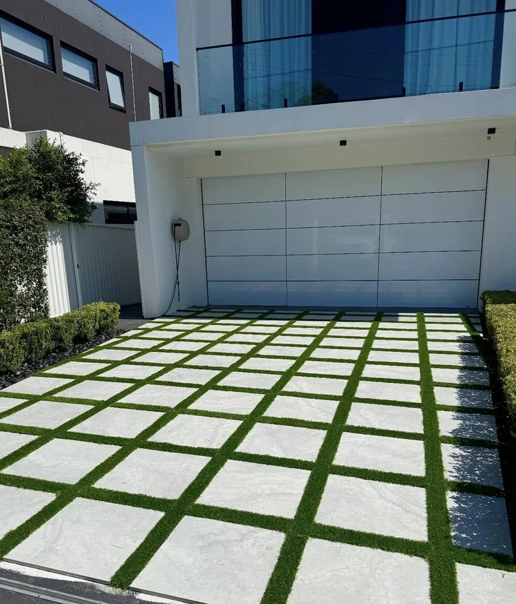 OneGrass synthetic grass strips between modern driveway pavers in front of a luxury white residential garage