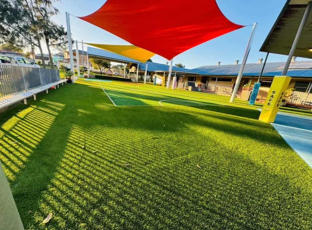 OneGrass multi-sport synthetic turf installed at a school playground featuring bright red and yellow shade sails