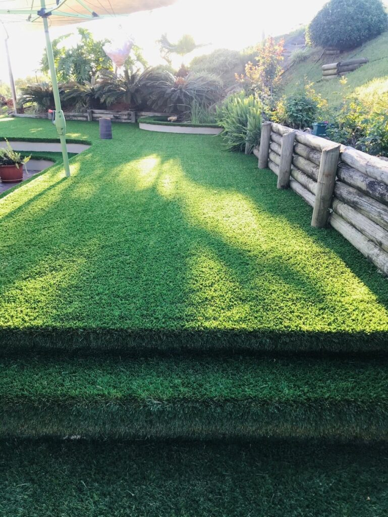 OneGrass synthetic turf installed on garden steps and tiered lawn areas in a lush, landscaped residential backyard