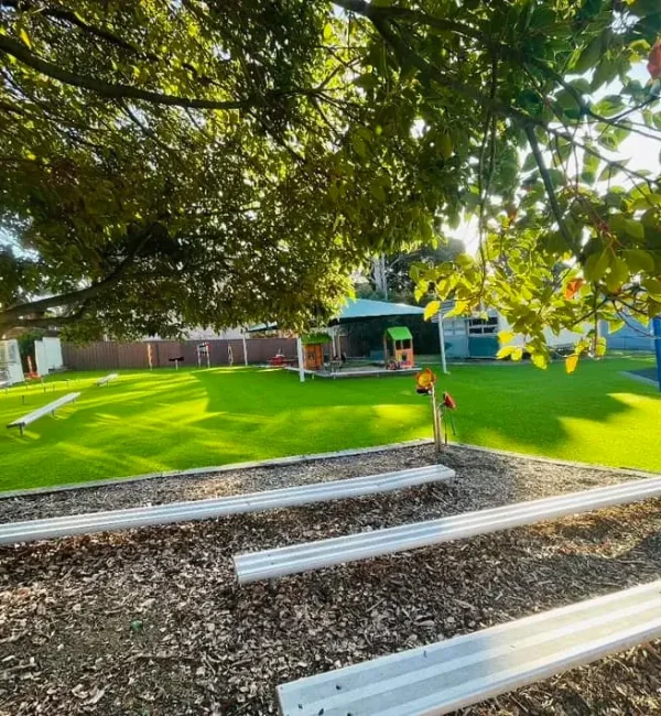 OneGrass artificial grass provides a lush, durable surface for a sunny school playground with benches and shade trees