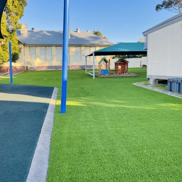 Expansive OneGrass synthetic grass installed in a playground with green shade sails and play equipment
