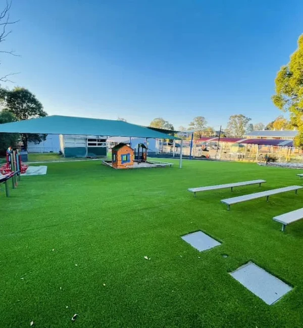 OneGrass synthetic turf creates a lush, low-maintenance lawn for a school playground with playhouses and shade sails