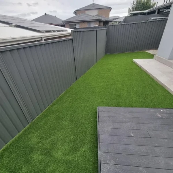 OneGrass synthetic turf provides a lush, low-maintenance lawn for a residential backyard with grey metal fencing