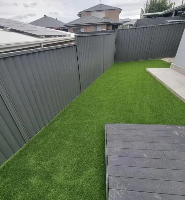 OneGrass synthetic turf provides a lush, low-maintenance lawn for a residential backyard with grey metal fencing