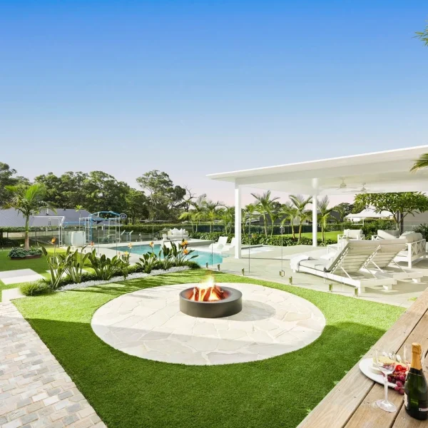 Luxury outdoor entertaining area featuring OneGrass synthetic turf, a stone fire pit, and a white modern cabana
