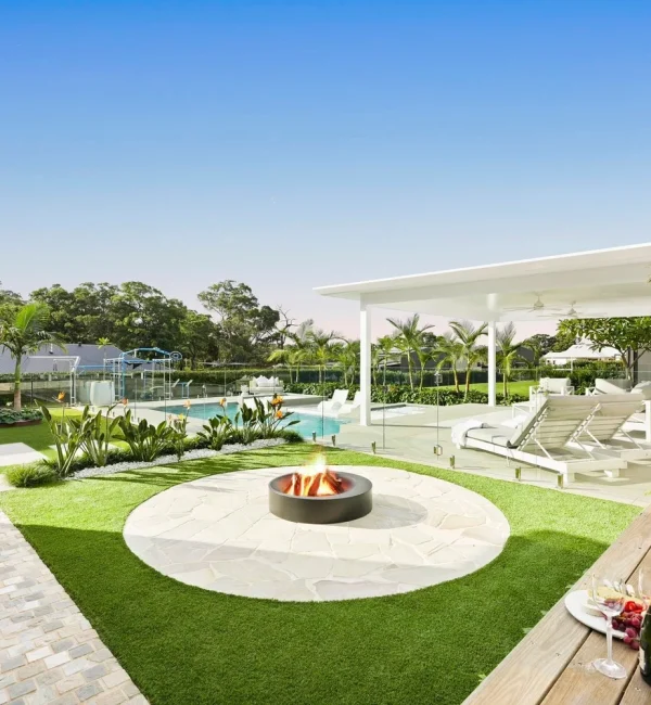 Luxury outdoor entertaining area featuring OneGrass synthetic turf, a stone fire pit, and a white modern cabana