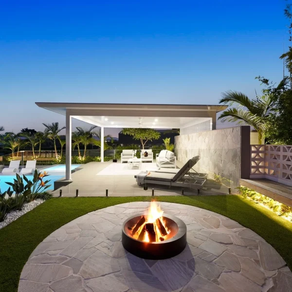 Luxury poolside entertaining area featuring OneGrass synthetic turf, a stone fire pit, and a modern white cabana