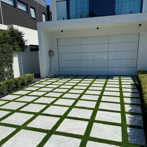 OneGrass synthetic grass strips between modern driveway pavers in front of a luxury white residential garage