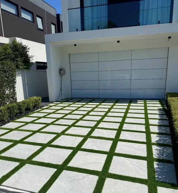 OneGrass synthetic grass strips between modern driveway pavers in front of a luxury white residential garage