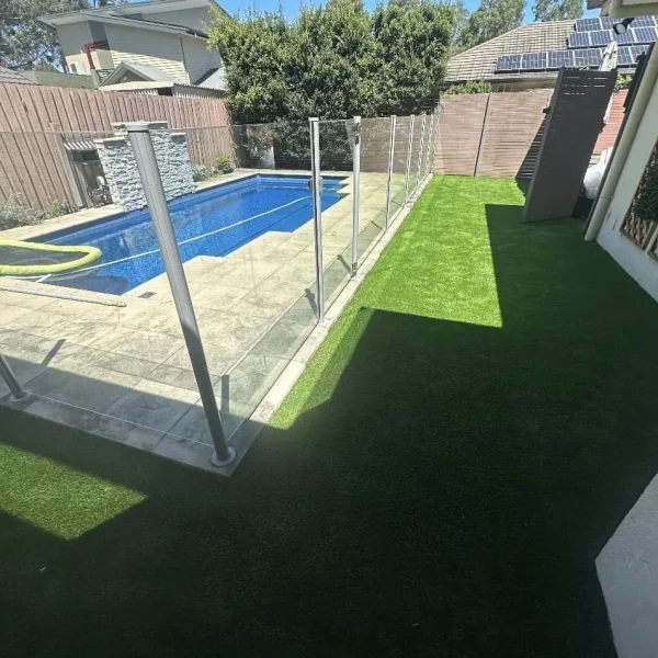 OneGrass synthetic turf creates a pristine, low-maintenance lawn beside a glass-fenced swimming pool