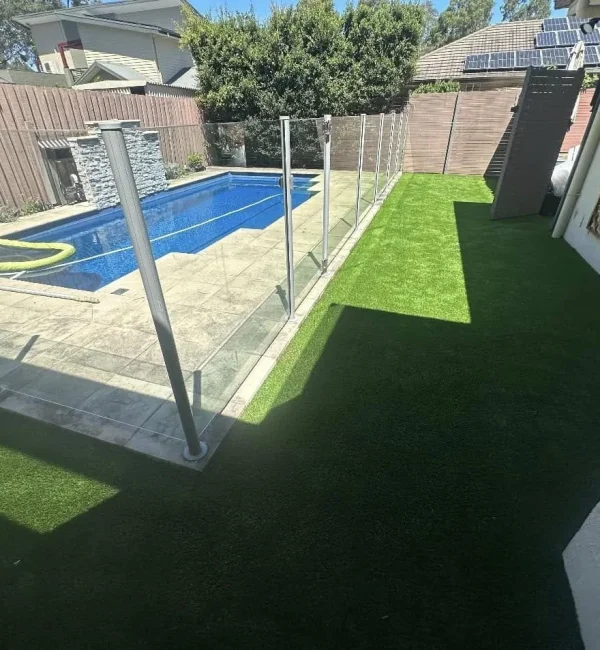 OneGrass synthetic turf creates a pristine, low-maintenance lawn beside a glass-fenced swimming pool