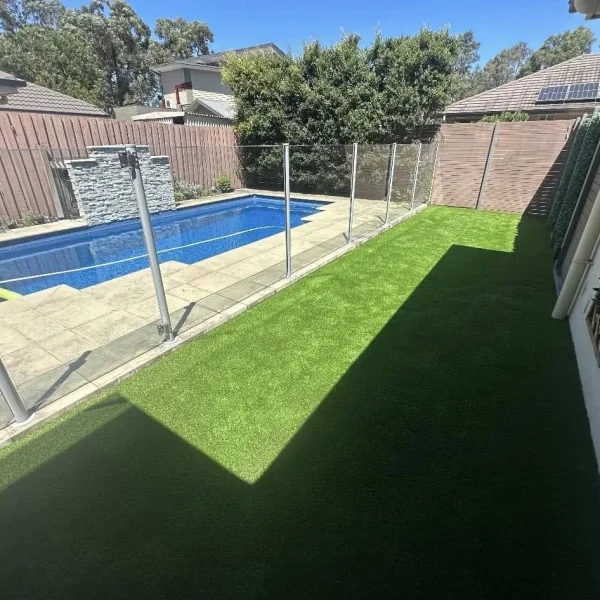 OneGrass synthetic turf creates a pristine, low-maintenance lawn beside a glass-fenced swimming pool