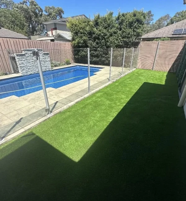 OneGrass synthetic turf creates a pristine, low-maintenance lawn beside a glass-fenced swimming pool