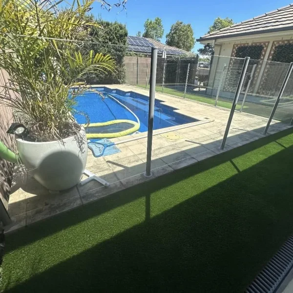 OneGrass synthetic turf creates a pristine, low-maintenance lawn beside a glass-fenced swimming pool