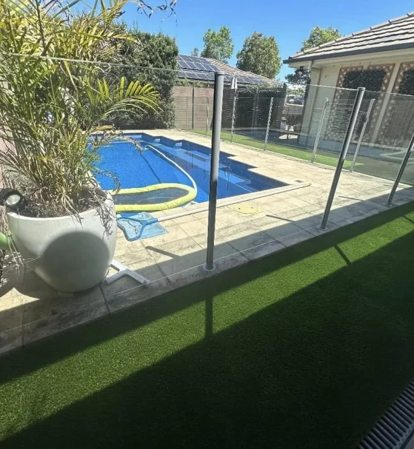 OneGrass synthetic turf creates a pristine, low-maintenance lawn beside a glass-fenced swimming pool