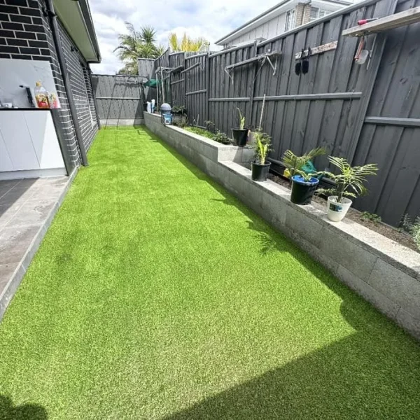 OneGrass synthetic turf creates a tidy, low-maintenance side yard lawn alongside a grey timber fence
