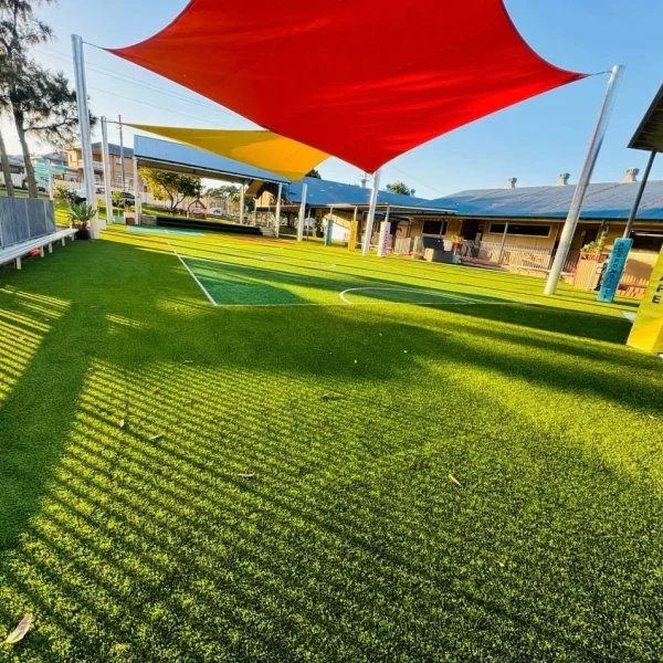 OneGrass multi-sport synthetic turf installed at a school playground featuring bright red and yellow shade sails