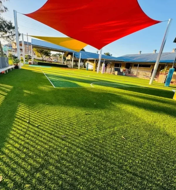 OneGrass multi-sport synthetic turf installed at a school playground featuring bright red and yellow shade sails