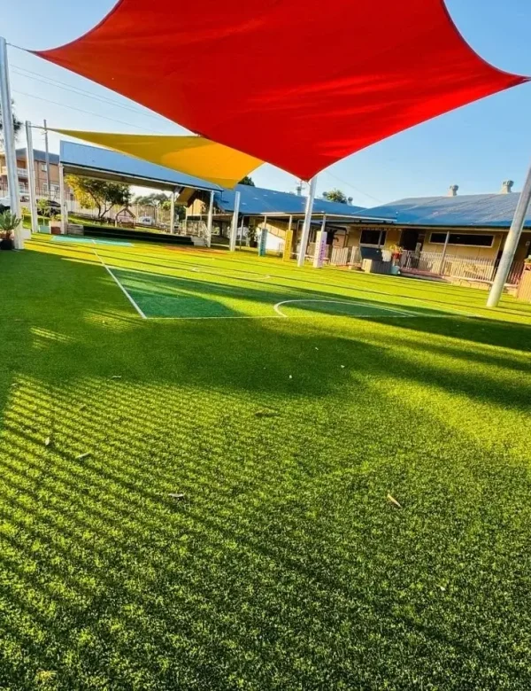OneGrass multi-sport synthetic turf installed at a school playground featuring bright red and yellow shade sails