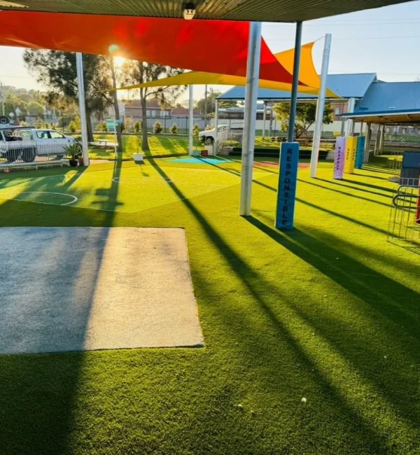 OneGrass multi-sport synthetic turf installed at a school playground featuring bright red and yellow shade sails