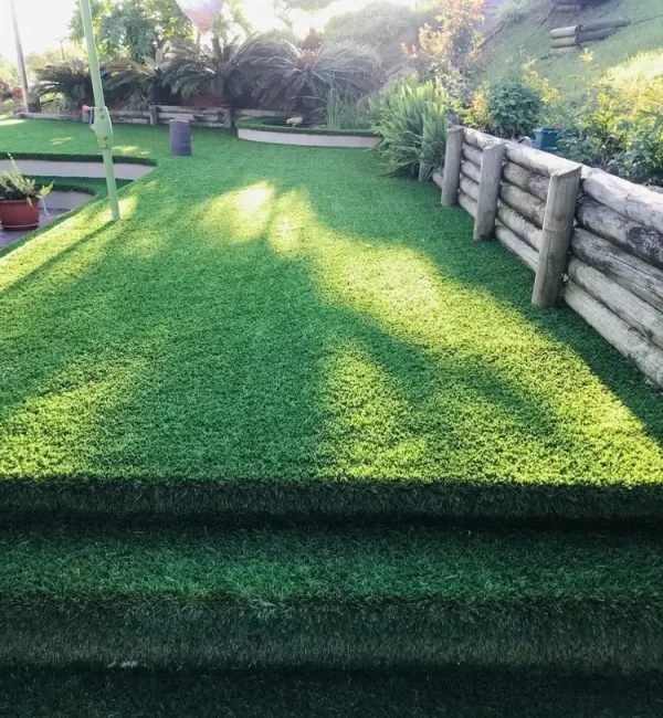 OneGrass synthetic turf creates seamless garden steps leading to a lush, tiered backyard lawn with timber retaining walls