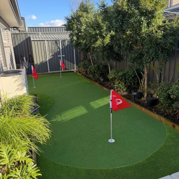 OneGrass premium synthetic turf installed in the backyard with red flags and fringe in a landscaped garden