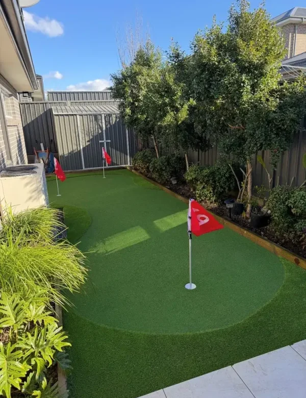 OneGrass premium synthetic turf installed in the backyard with red flags and fringe in a landscaped garden