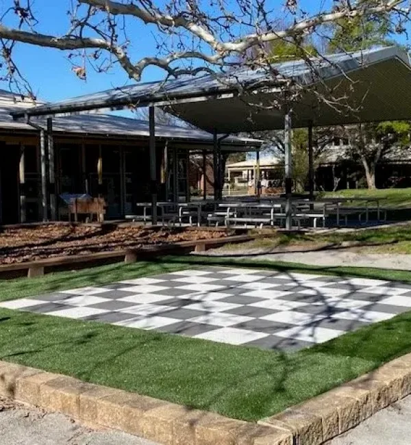 OneGrass synthetic turf borders a giant outdoor chessboard in a paved school courtyard area under a large canopy