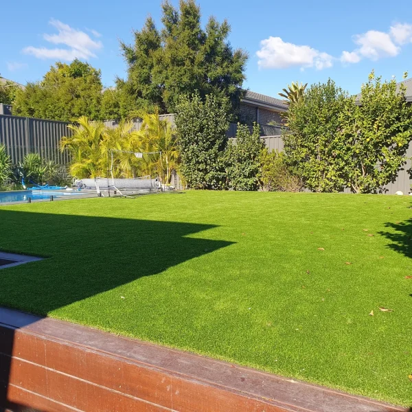 Lush OneGrass synthetic turf creates a vibrant, level backyard lawn beside a swimming pool and timber decking