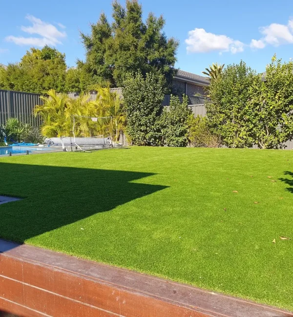 Lush OneGrass synthetic turf creates a vibrant, level backyard lawn beside a swimming pool and timber decking