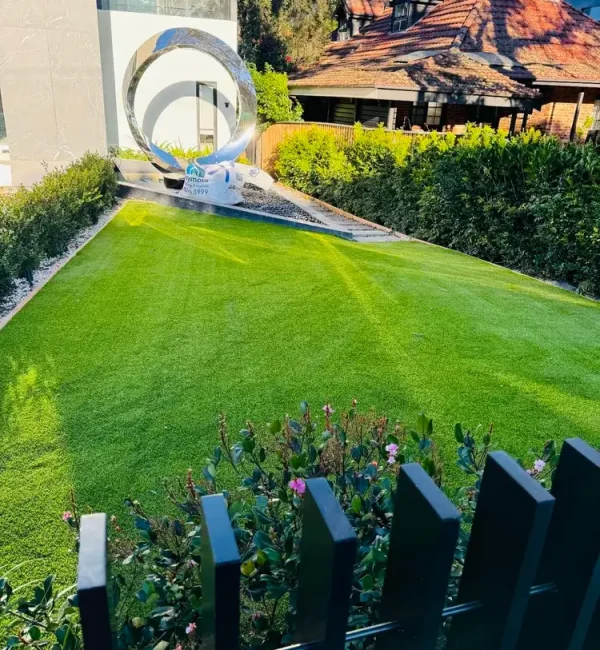 Lush OneGrass synthetic turf provides a pristine, sloped front lawn for a modern home with a silver ring sculpture