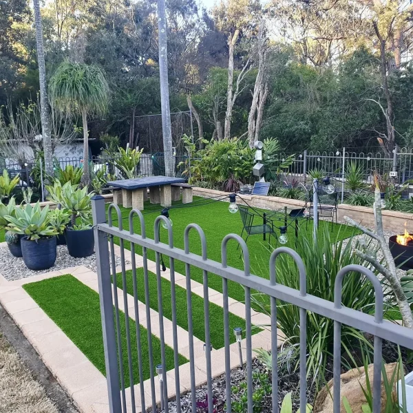OneGrass synthetic turf creates a modern backyard lawn featuring a fire pit, stone table, and agave planters