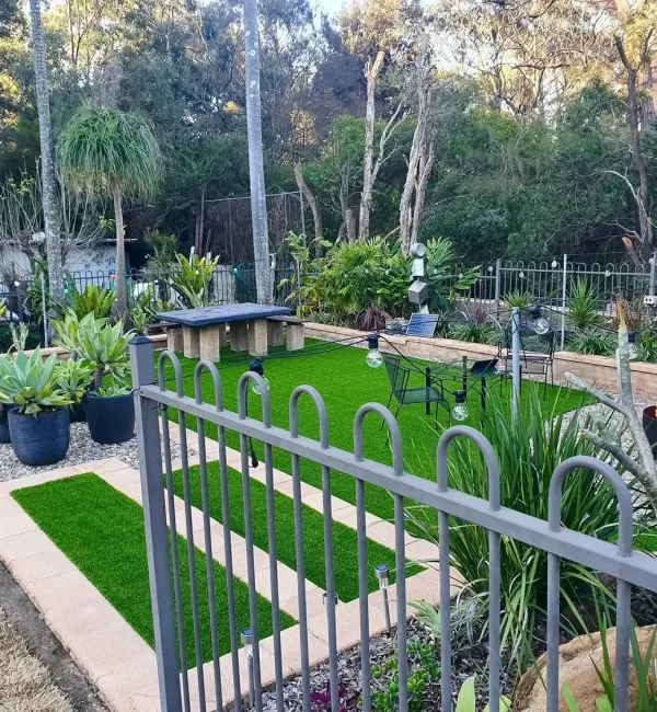 OneGrass synthetic turf creates a modern backyard lawn featuring a fire pit, stone table, and agave planters