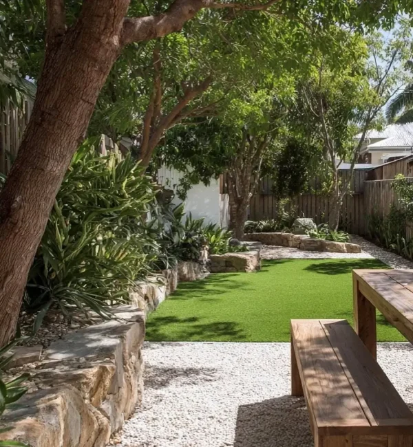 A timber picnic table and bench sit on a gravel path beside a lush OneGrass synthetic turf lawn and stone retaining wall