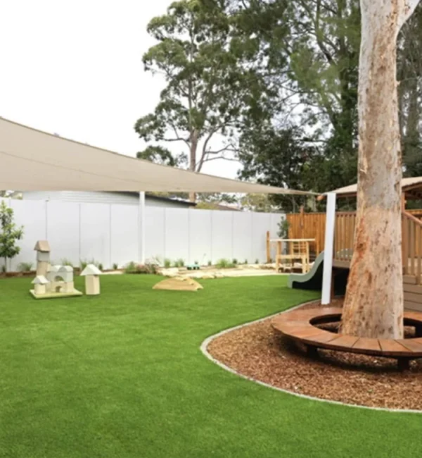 OneGrass synthetic turf surrounds a large gum tree with circular timber seating in a playground