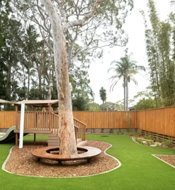 OneGrass synthetic turf surrounds a large gum tree with circular timber seating in a playground