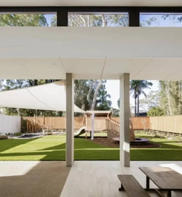 Wide view of a play area featuring OneGrass synthetic turf, shade sails, and timber picnic seating