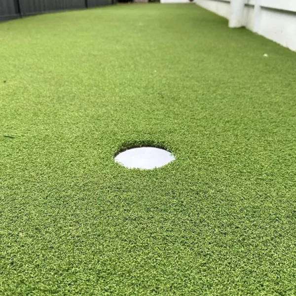 Close-up of a premium OneGrass synthetic turf with a golf hole cup installed in a narrow side garden