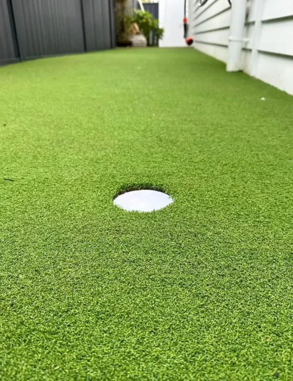 Close-up of a premium OneGrass synthetic turf with a golf hole cup installed in a narrow side garden